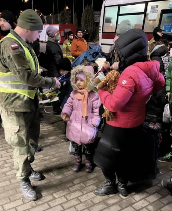 A Ukrainian child and her mother interact with an emergency official outside the buses, courtesy of Jake Knotts