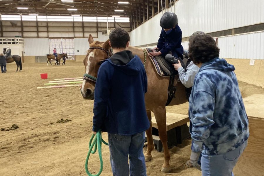 Volunteer+Samantha+Clark+and+another+volunteer+watch+as+client+Rohan+Kamath-Rayne+receives+help+getting+on+the+horse+from+his+therapist.