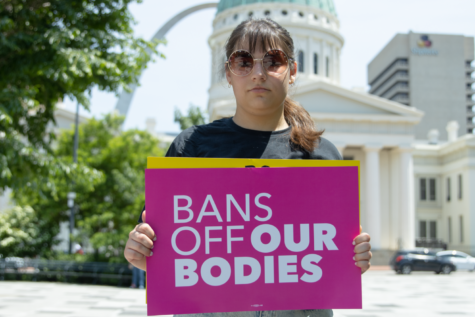 Senior Athena Widlacki stands in front of the St. Louis Arch on Kiener Plaza, with one of the free %23BansOffOurBodies posters.