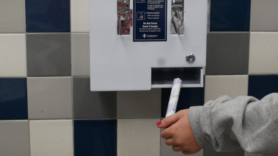 A+student+receiving+a+tampon+from+the+newly+installed+period+product+dispensers.+