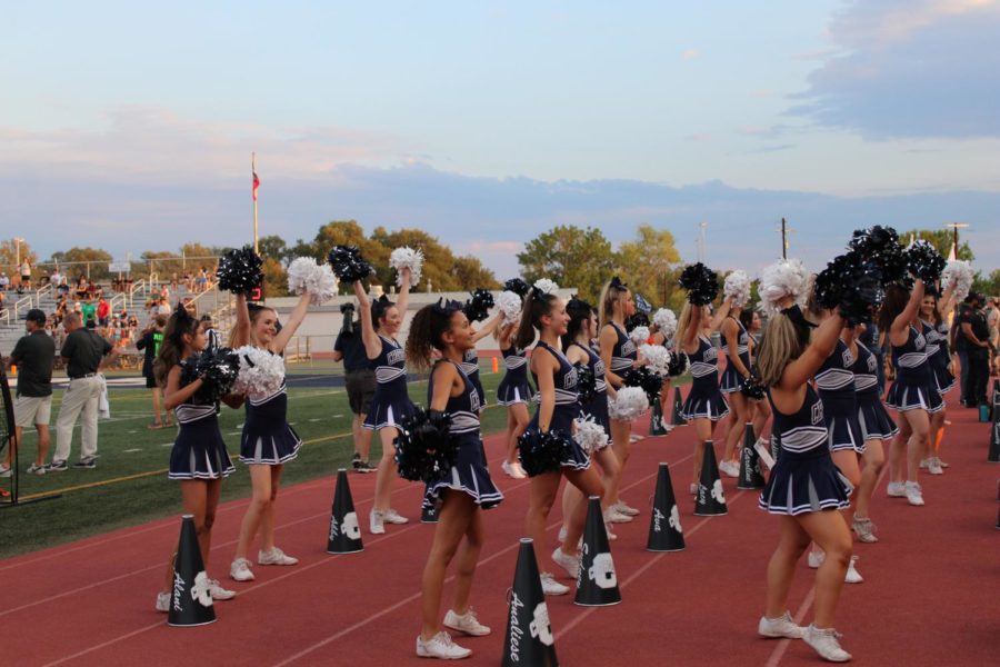 Cheerleaders performing for the student section during a home varsity football game this fall. Often some of the first to arrive and last to leave, the cheer team typically spends every hour from the end of school to midnight on football Fridays practicing, setting up, performing, and traveling.