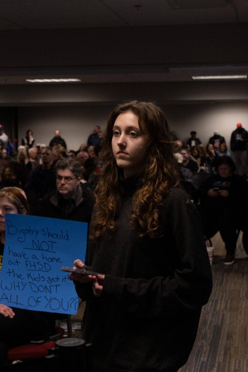 A+student+stands+next+to+a+sign+that+protests+the+board+decision+during+the+Board+of+Education+meeting.+The+decision+was+highly+controversial+and+caused+many+people+to+rally+against+the+decision.+