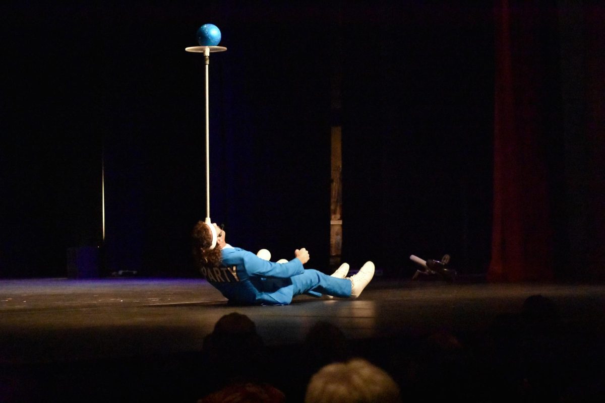 Game of Throws gala-show performer Mark Wilder lowers himself to the ground and raises himself back up while balancing a ball atop a pole on his forehead. 