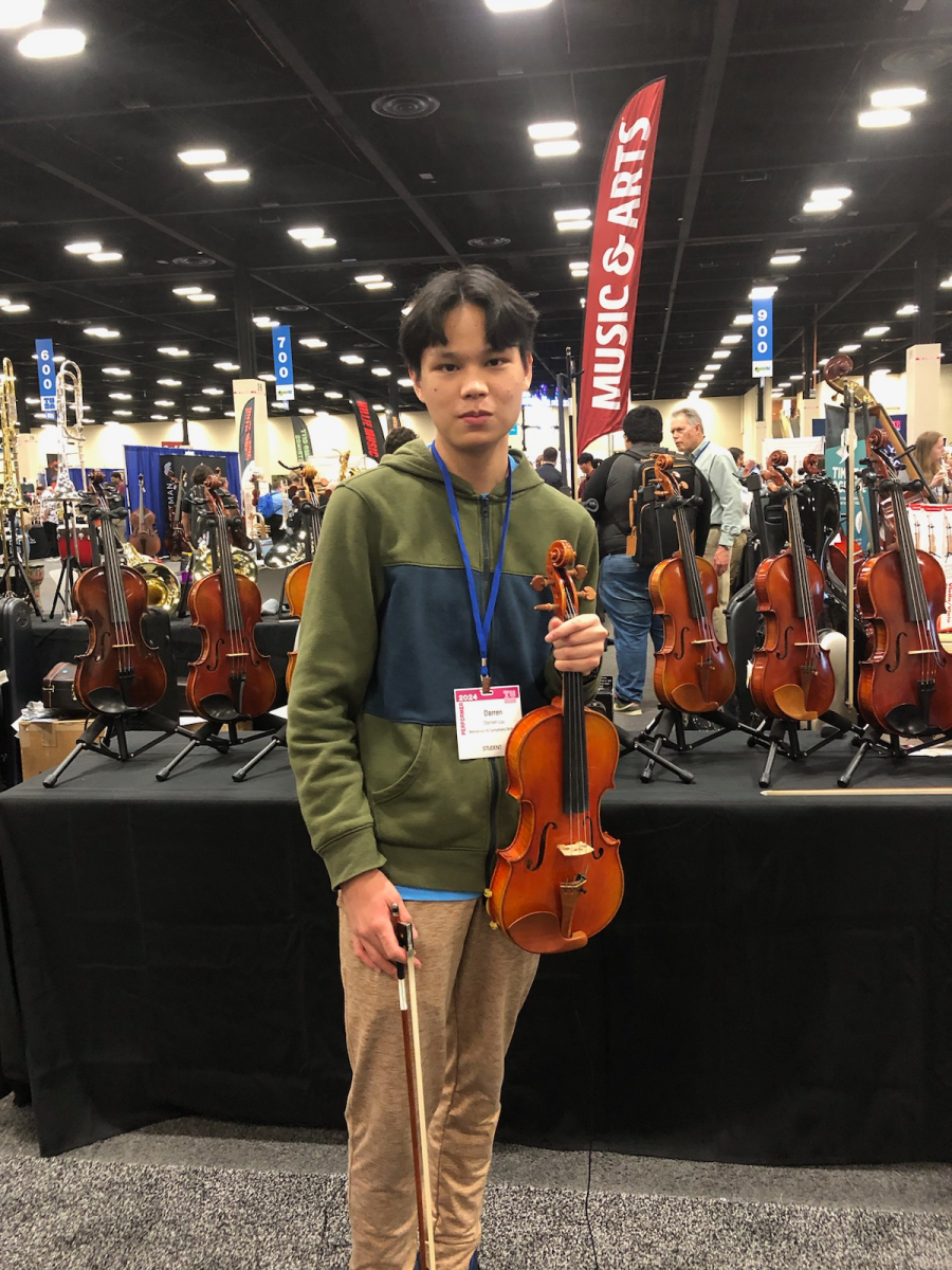 Violinist Darren Liu 24 stands in front of a row of violins on display at the Texas Music Educators Association (TMEA) convention. Westwoods Symphony Orchestra was invited to TMEA for an honors recital because they were recognized as the best orchestra in Texas.