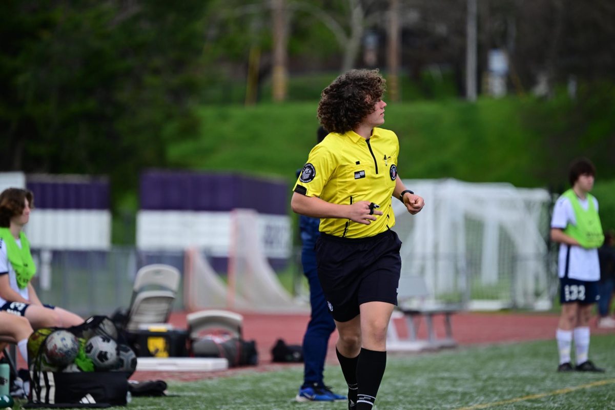 A referee sprints down the sideline, while officiating a soccer game.