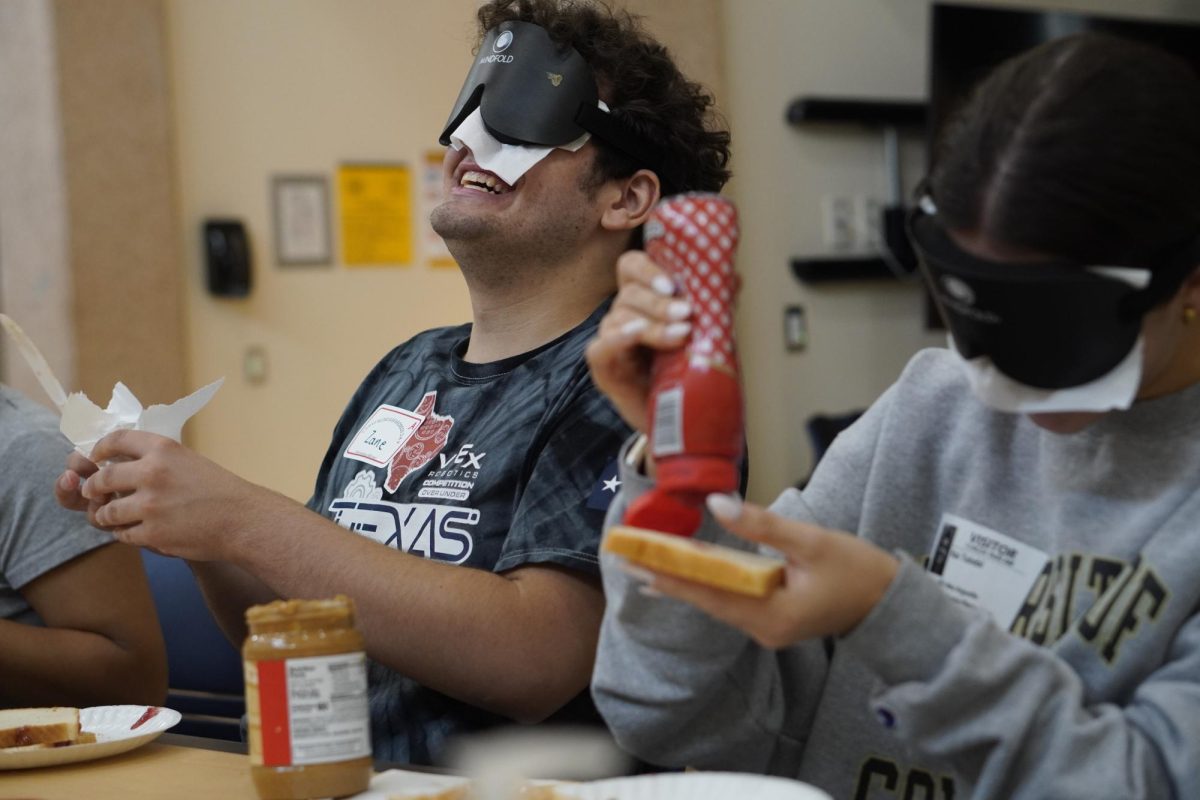 AS EASY AS PB&J: At the blindfold sandwich-making station, senior Zane Wiggins and Kai Talebi attempt to make a peanut butter and jelly sandwich. The activity allowed students to experience the mundane task without sight. Wiggins found that the simple activity turned into a challenge in almost every aspect of the process.

"It was pretty rough," he said. "My bread wasn’t put together properly, and I put my jelly right next to my plate and not on the plate, it was really difficult. I was expecting it to be easier than it was cause I'd made sandwiches all my life, and I thought 'I can do this from muscle memory,' but it was a lot harder than I thought, and it makes you not take your sight for granted. Access to your sight makes things so much easier."

Since students participating are used to having full sight, it was difficult to adapt to the sudden loss of a sense.

"I had to kind of guess where things were and the plate was moving a lot," he said. "Every time I would reach for the plate it would be in a different location, so I kind of had to feel around for everything."

Along with that, Wiggins had to work together with Talebi to communicate to communicate which ingredient he needed next.

"I had to share the peanut butter and the jelly with Kai, so we had to coordinate with each other on who gets what first," he said. "I knew Kai was right next to me, but it was hard to know where her hands were. We had to find each other's arm and make our way up to pass the ingredients."

Caption by Lillian Gray.