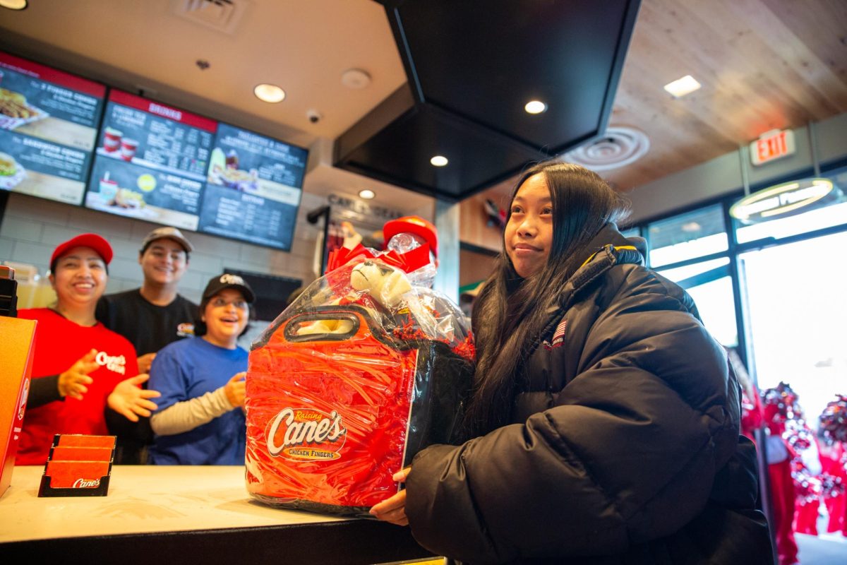 Kristina Cruz, the first customer at the new Raising Cane’s restaurant in Colma, Calif., poses with a gift basket as employees cheer during the restaurant's opening on Tuesday, Nov. 19, 2024. (Dan Hernandez / Golden Gate Xpress)