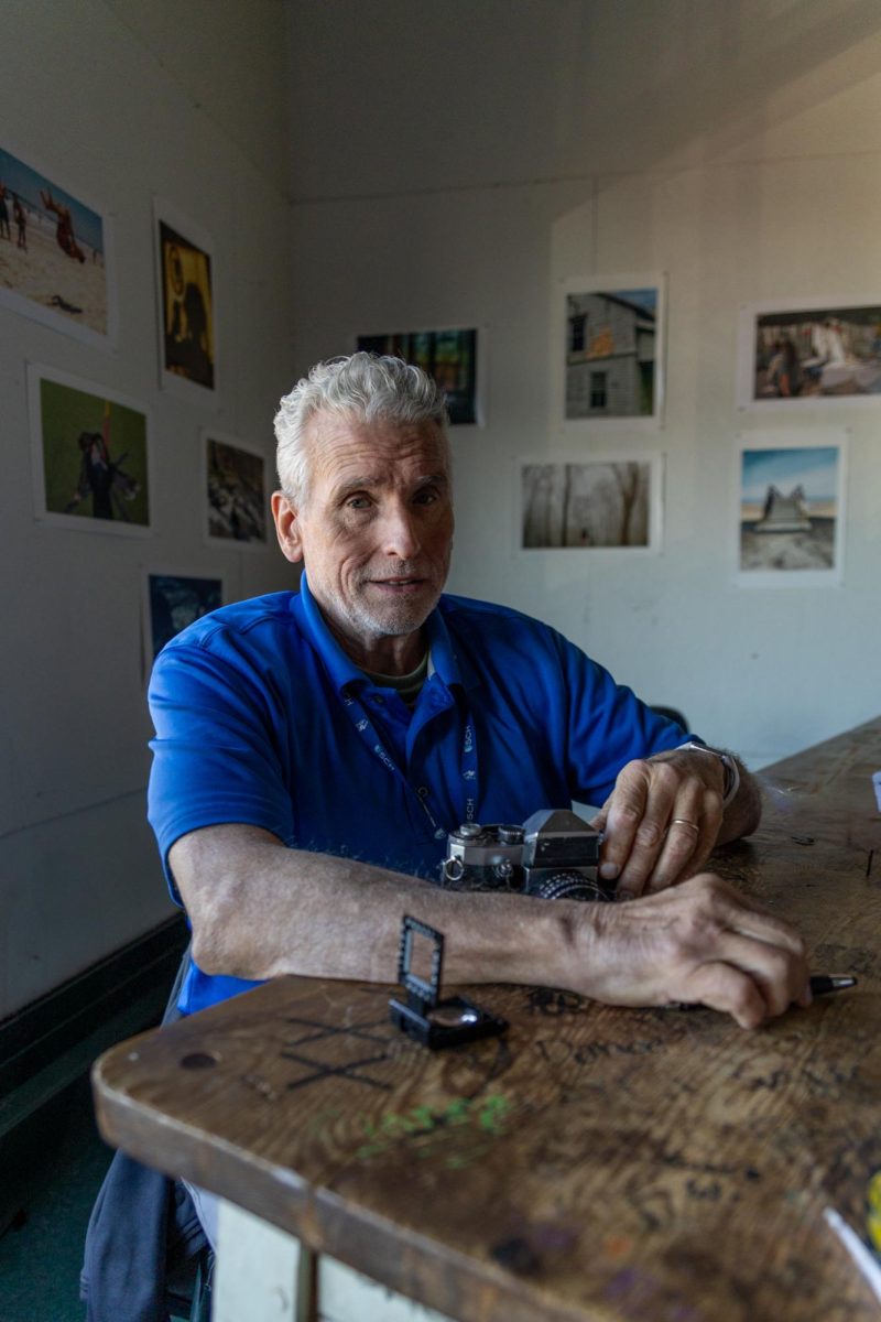 Pete Capano holds camera while working at his desk.