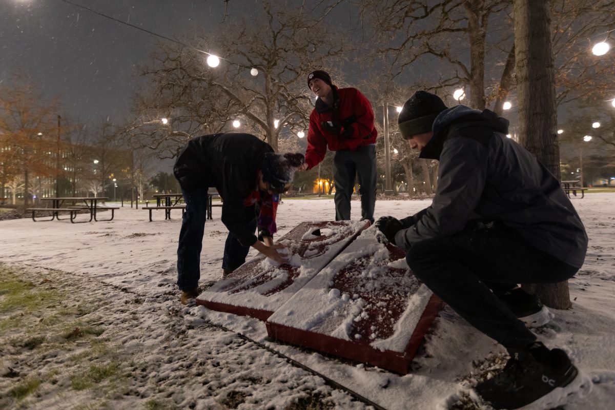 Engineering freshman Pablo Murura, engineering freshman Travis Reed and business freshman Maddox McMinn scoop snow from cornhole boards at Aggie Park on the morning of Tuesday, Jan. 21, 2025. (Chris Swann/The Battalion)