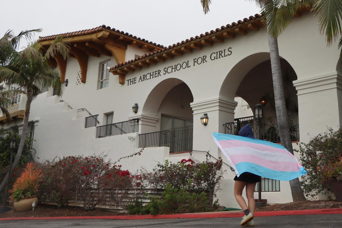 An upper school student walks in the front of the school, wearing a transgender flag on their back. In President Trump's inauguration speech, he declared that "there are only two genders: male and female." During this time, transgender and nonbianary Archer students aim to educate the community and fight against gender inequality.