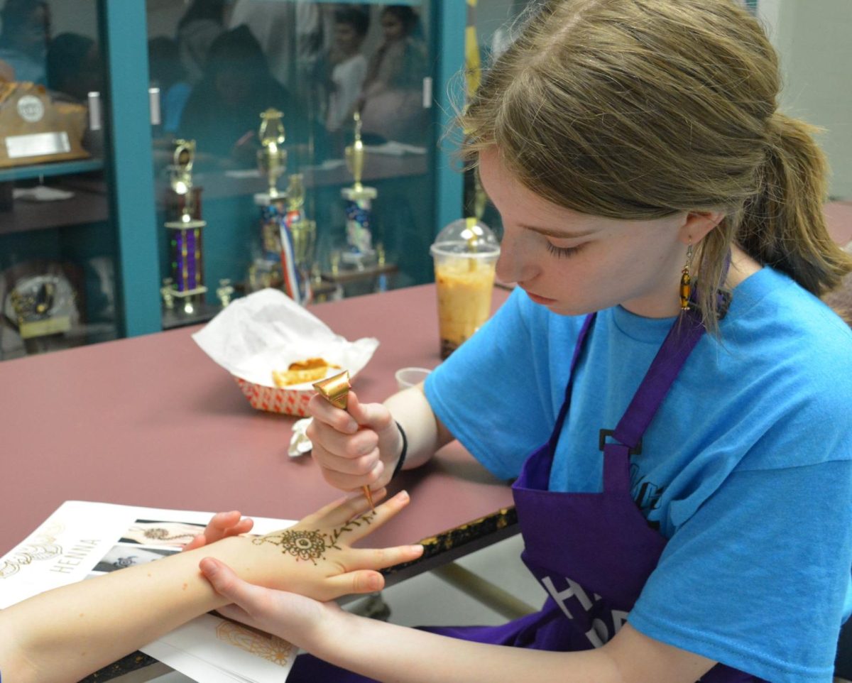 Sophomore Clare Colburn draws a henna design on a child's hand. Henna designing was one of the activities for guests, and art students were able to sign up for different activities they could do during the art show. “One of my favorite activities was Henna because it's a really cool craft and art form that is interesting,” Colburn said. 