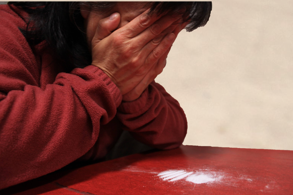 An individual struggling with addiction sits in despair over whether or not to continue with this lifestyle. Cocaine, a highly addictive party drug lies in lines in front of them.
