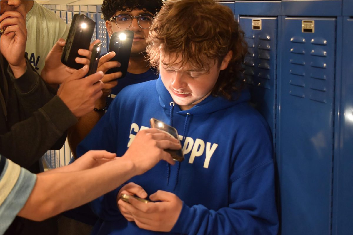 Senior JT Barrett is surrounded by classmates holding up their phones—an exaggerated but all-too-familiar reflection of how overwhelming screen culture can feel. (Image has been upscaled in Photoshop)