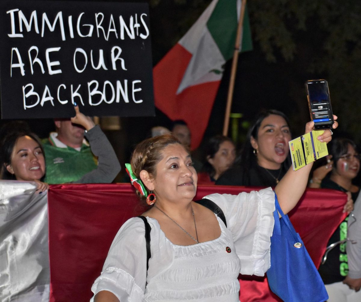 Holding up her phone to capture the moment, a woman joins neighbors on Sept. 16 in West Chicago, where chants and signs declared “Immigrants are our backbone.” The protest, timed with Mexican Independence Day celebrations, became both a march for pride and a stand against ICE raids.