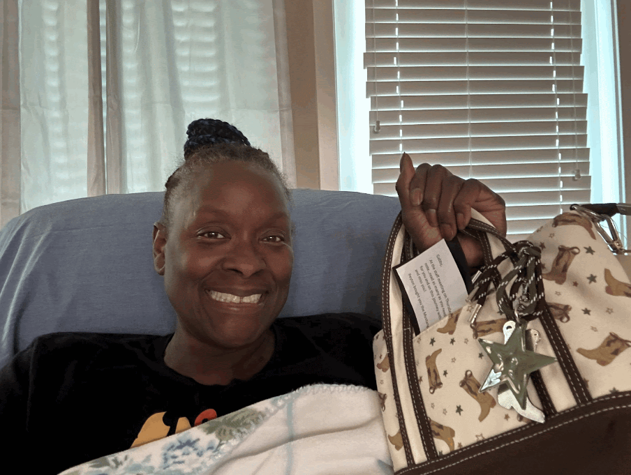 Ms. Stephenson at home, smiling through her treatment and holding up a gift from a student.
