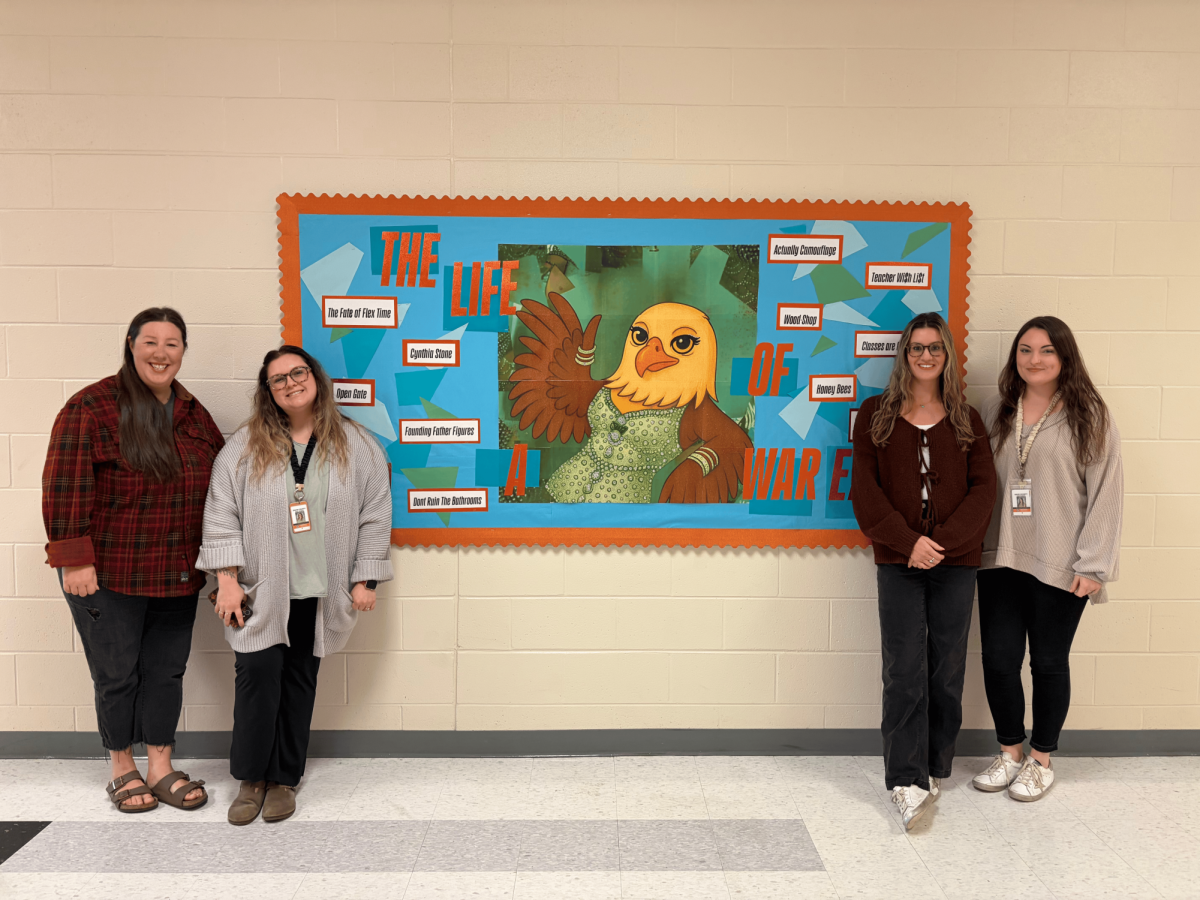 (Left to Right) Megan Baker, Kamryn Harris, Laura Doub, and Meranda Shoemaker pose in front of the "Life of a War Eagle" bulletin board they designed as part of their annual tradition of creating Taylor Swift-themed boards to display in the third-floor history hallway.