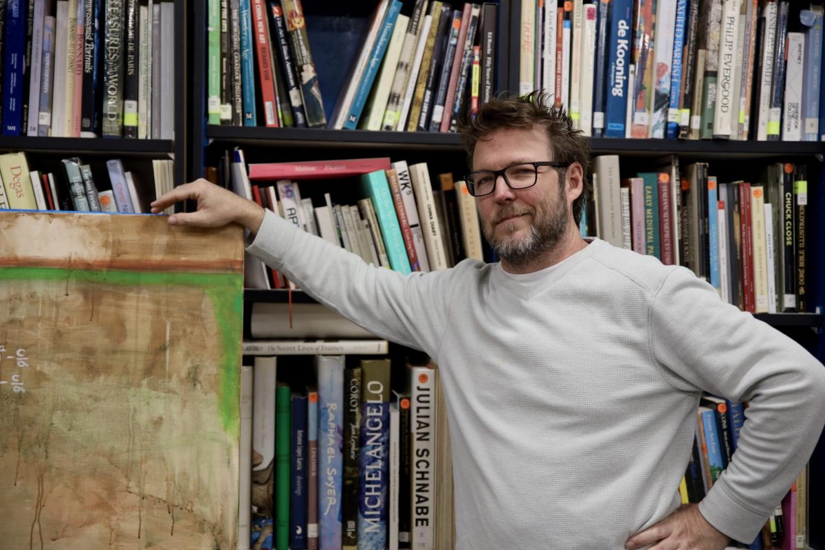 Visual teacher Ryan Toth stands before an extensive collection of artist books, available to students, alongside his own original works displayed around the classroom, as both guidance and inspiration for the students’ own artwork.